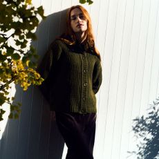 Model leaning against a garden fence wearing a green Finery London cardigan