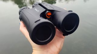 Celestron Outland X 10x42 being handheld in one hand over a lake water