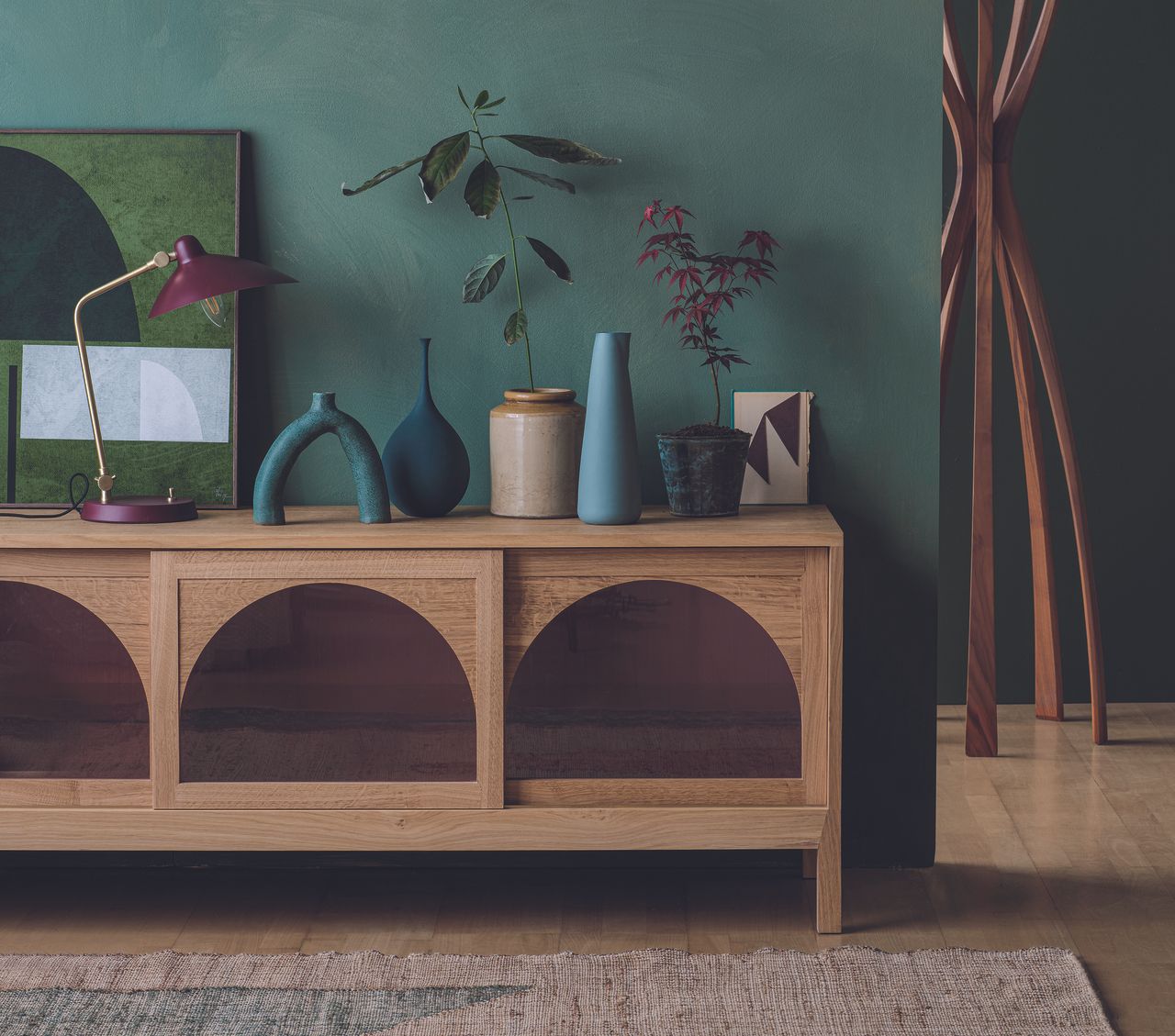 A room painted in emerald green with a natural rug and a wooden sideboard 