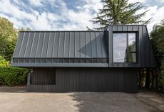 The living quarters of the compact house are set above a wood-clad ground floor containing the garage