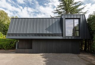 The living quarters are set above a wood-clad ground floor containing the garage