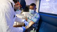 health care worker in an n95 mask prepares to give a vaccine into the forearm of a young man wearing a surgical mask