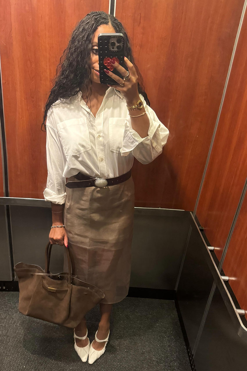 A woman wearing a white button shirt, tan pencil skirt, white pointed-toe heels, and a tan handbag