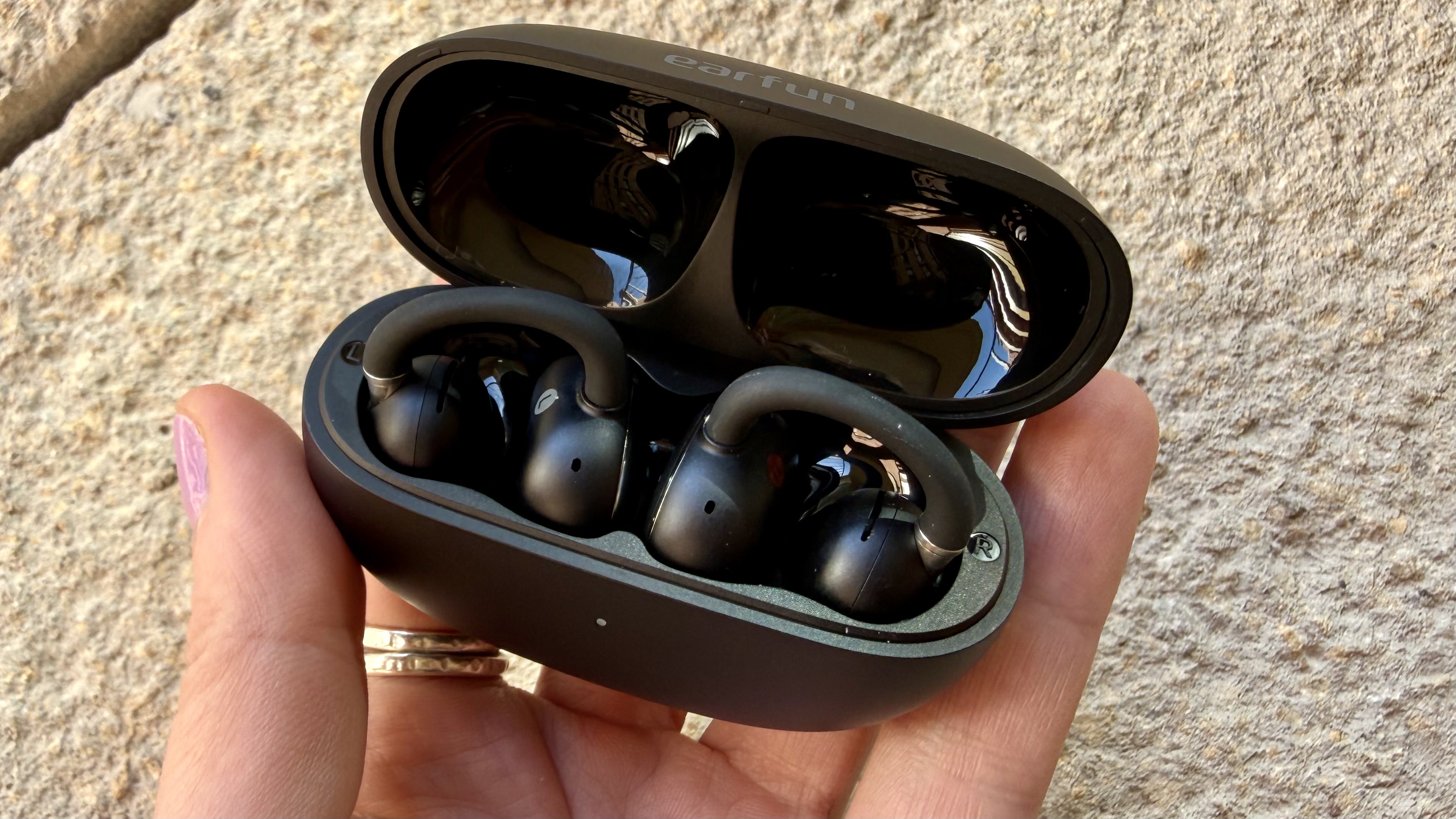 Someone holding the EarFun Clip 2 earbuds in their charging case