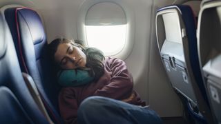 A woman with dark hair curls up on a plane seat to sleep during the flight as advised by a sleep expert for getting over jet lag