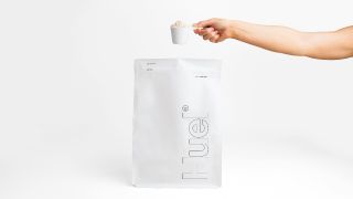 A hand holding a scoop of Huel Essential meal replacement powder