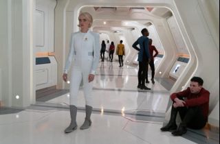 a woman in a white body suit in a white hallway with people in the background