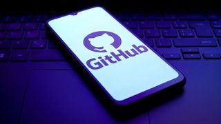 GitHub logo on smartphone screen sitting on laptop keyboard with purple lighting