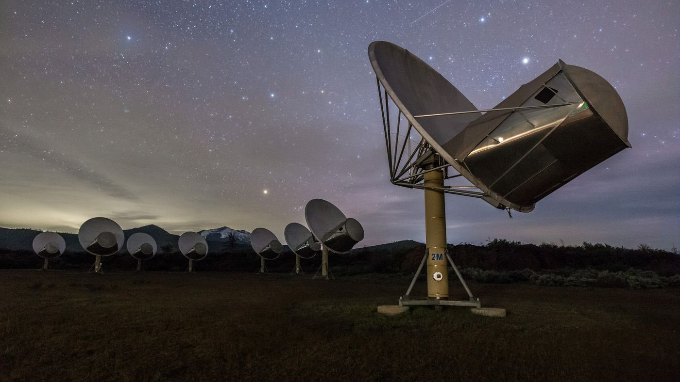 image of a dozen large radio dishes in an open field beneath a brilliant nighttime sky