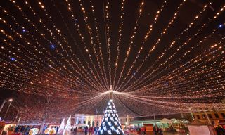A lit-up Christmas tree and overhead string lights at an outdoor market