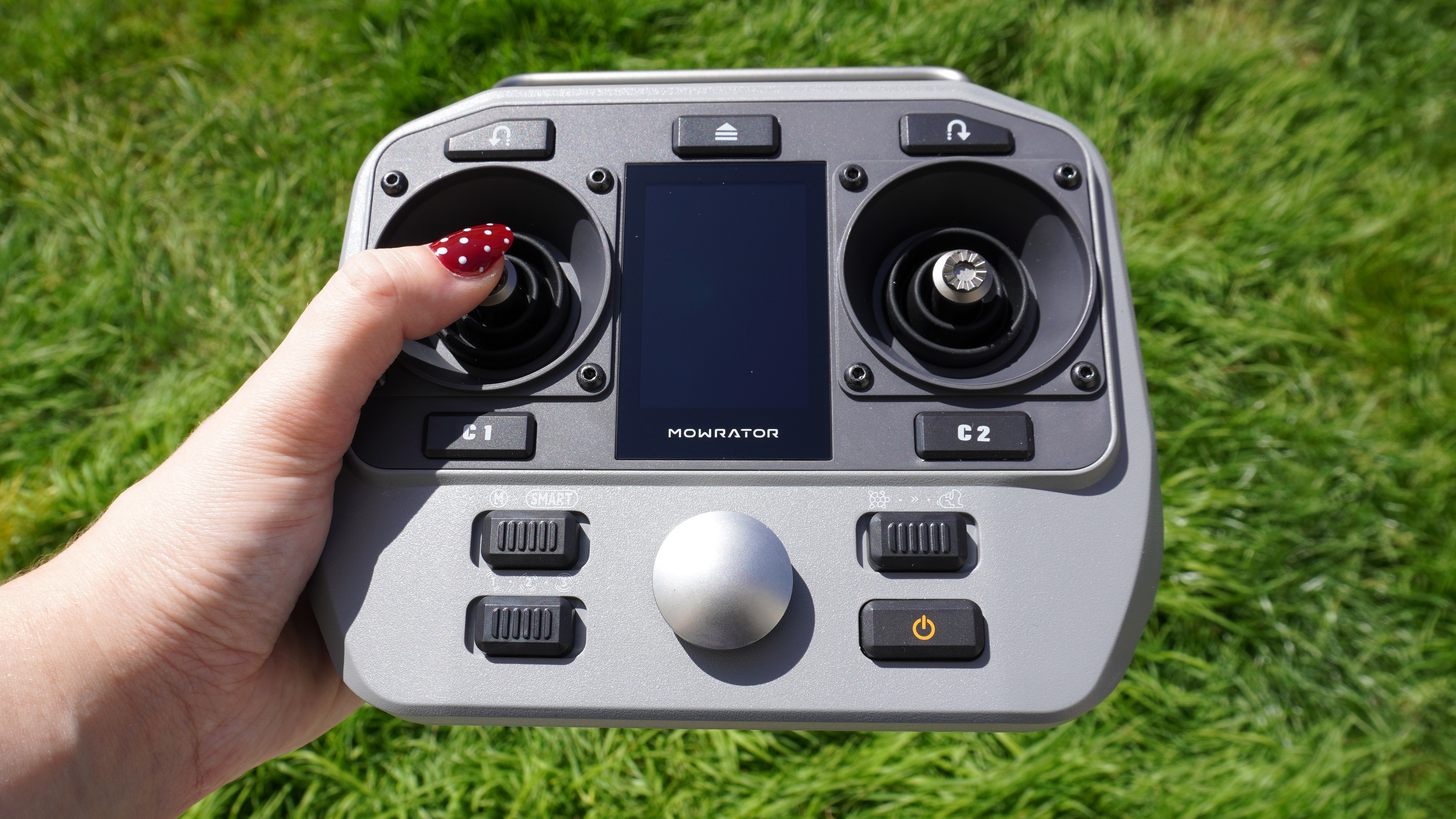 Hand holding the remote controller for the Mowrator S1 2WD lawnmower.