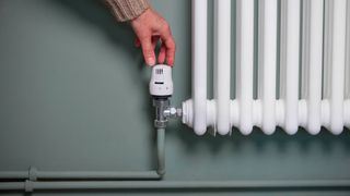green wall with white radiator and hand turning down thermostatic valve on radiator