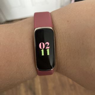 Fitbit Luxe worn on writer's hand with clock view