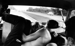 Black and white image of a couple kissing each other in a car.