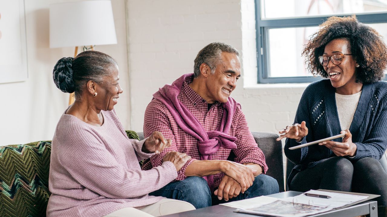 An older couple laugh and smile as their financial adviser explains something.