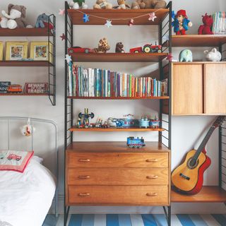 A kids room with a wall covered in storage furniture displaying toys and books