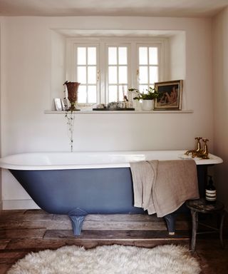 freestanding cast iron bath in a cottage bathroom with sheepskin rug on wooden floor