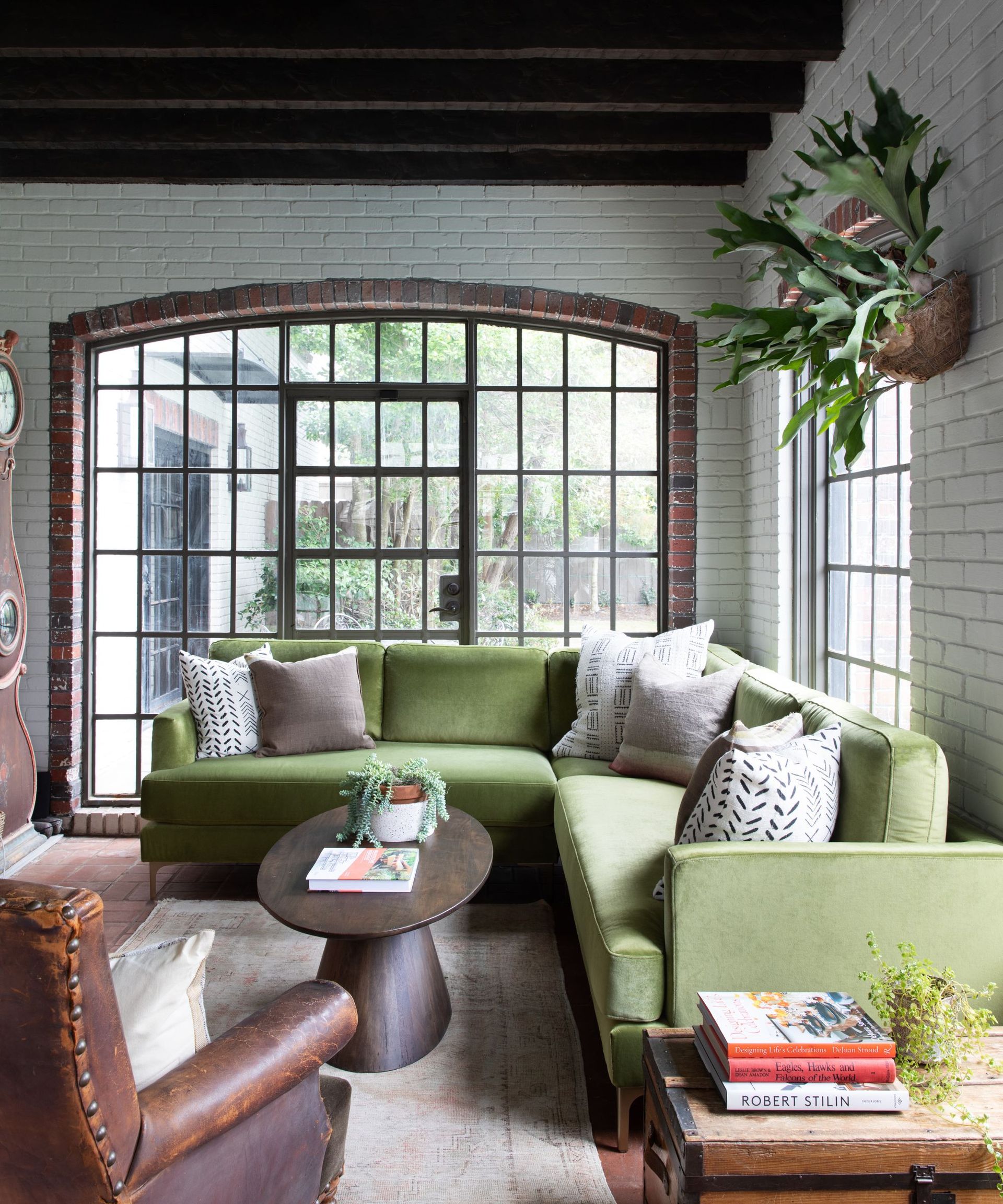 Exposed brick living room with beams and large green sectional sofa with leather armchairs and round coffee table