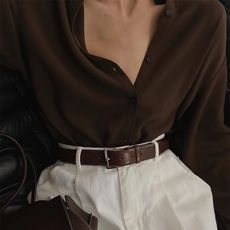 Woman wears brown shirt, cream trousers and brown belt