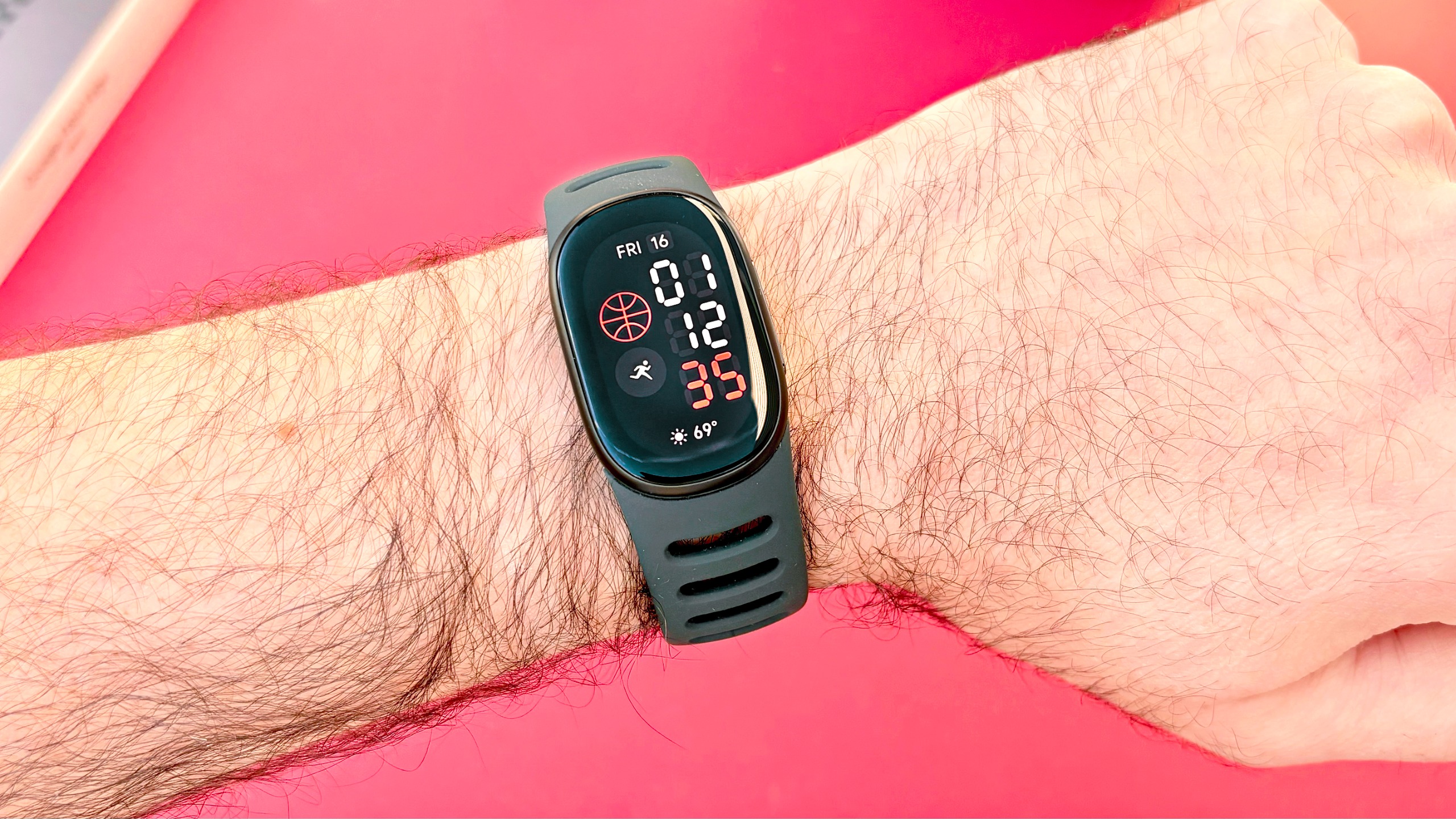 Close-up of the Fitbit Edge fitness tracker on the reviewers' wrist against a bright red background