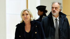 Marine Le Pen, wearing a black coat and gold necklace, and her lawyer, wearing a dark coat and tie, walk outside of a French courtroom