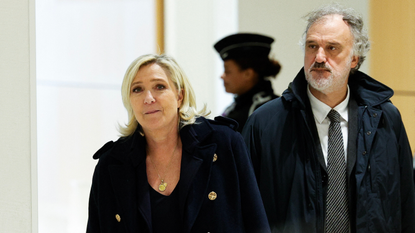 Marine Le Pen, wearing a black coat and gold necklace, and her lawyer, wearing a dark coat and tie, walk outside of a French courtroom