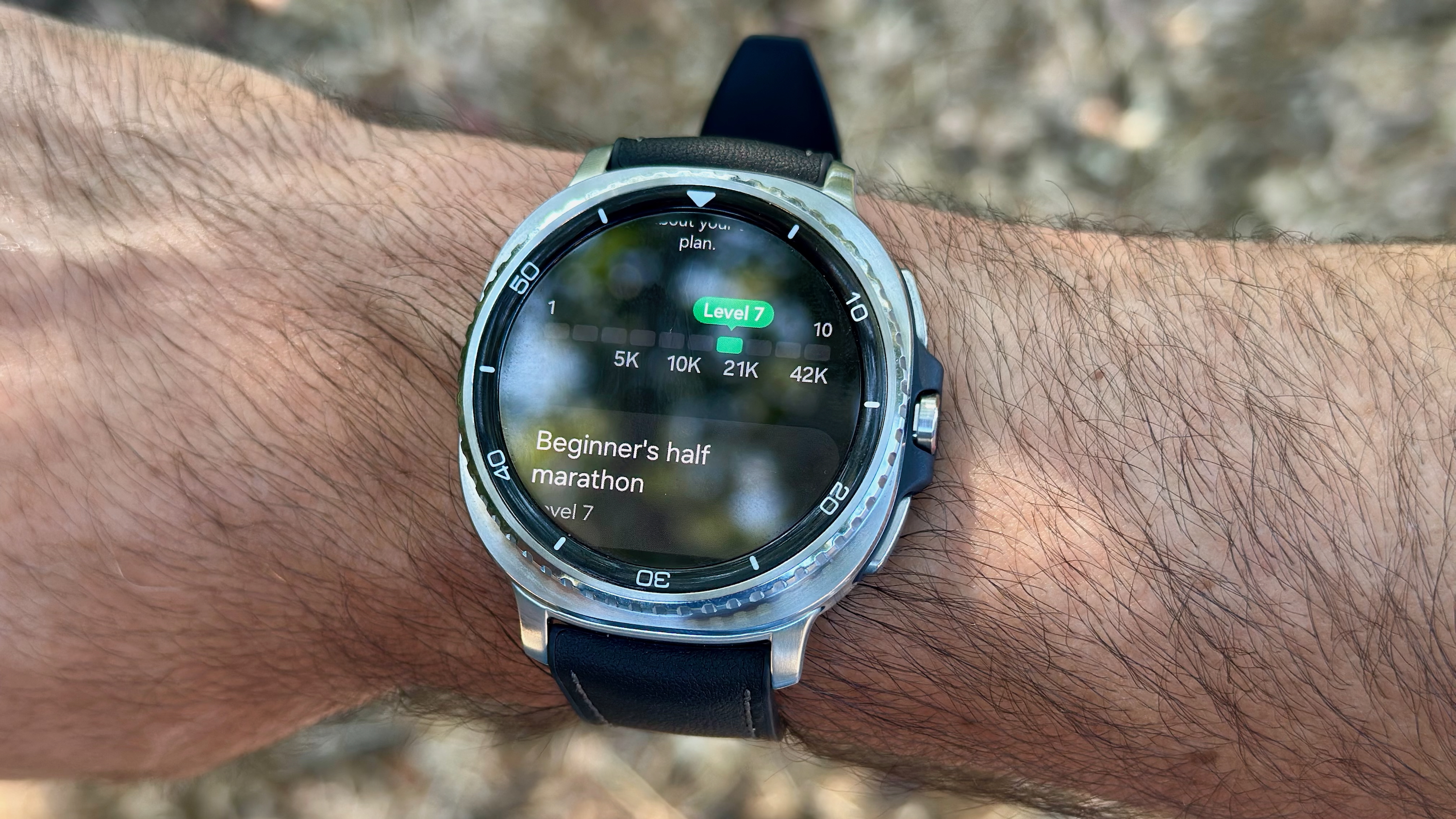 The Samsung Galaxy Watch 8 Classic worn on a wrist outside, the display showing where Level 7 ranks on a distance timeline and the words "Beginner's half marathon: Level 7" underneath.