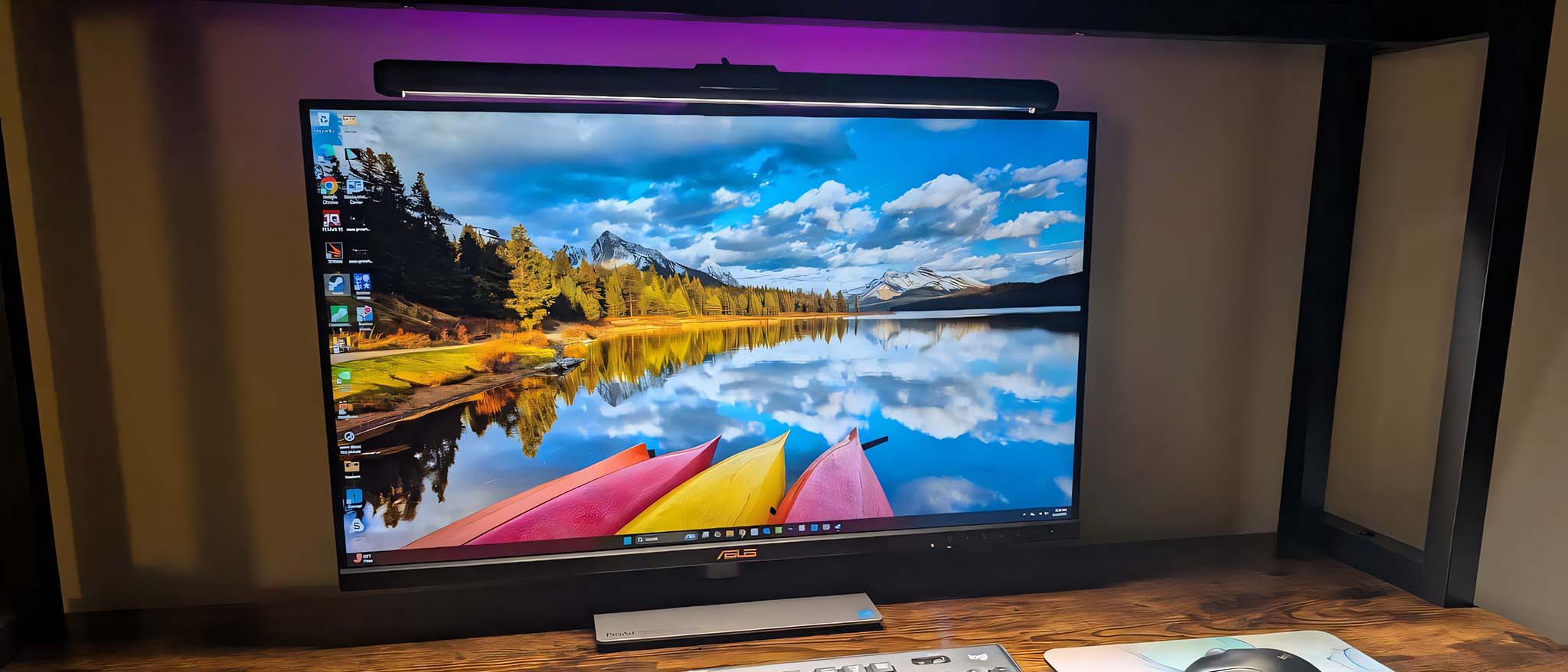 ASUS ROG Aura Monitor Light Bar emitting RGB lighting behind a monitor while shining LED white light on a keyboard and mouse. 