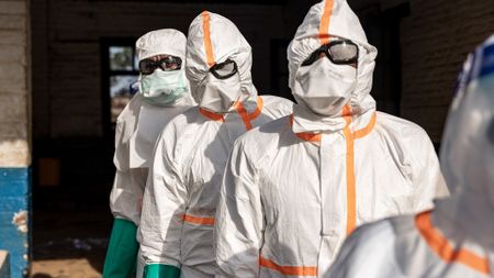 A series of people wearing white clean suits and goggles with masks.