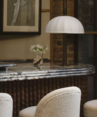 A marble countertop with white boucle bar stools and a domed light fixture