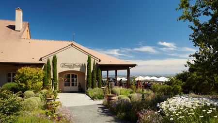 The exterior of Domaine Drouhin Oregon in the Willamette Valley, with flowers in the foreground and an outdoor tasting patio with umbrellas over the tables.