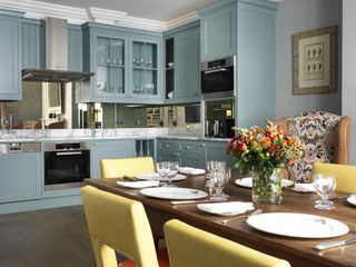 Baby blue kitchen cabinets and a bright dining area with buttermilk yellow chairs and a wooden table.