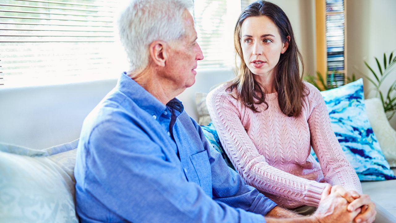 A woman and her father talking, sitting on a sofa at home