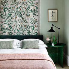 A bedroom with a botanical mural behind the bed made of green and pink accents