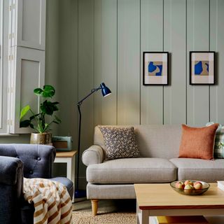 A living room with panelled walls in sage green with a grey sofa