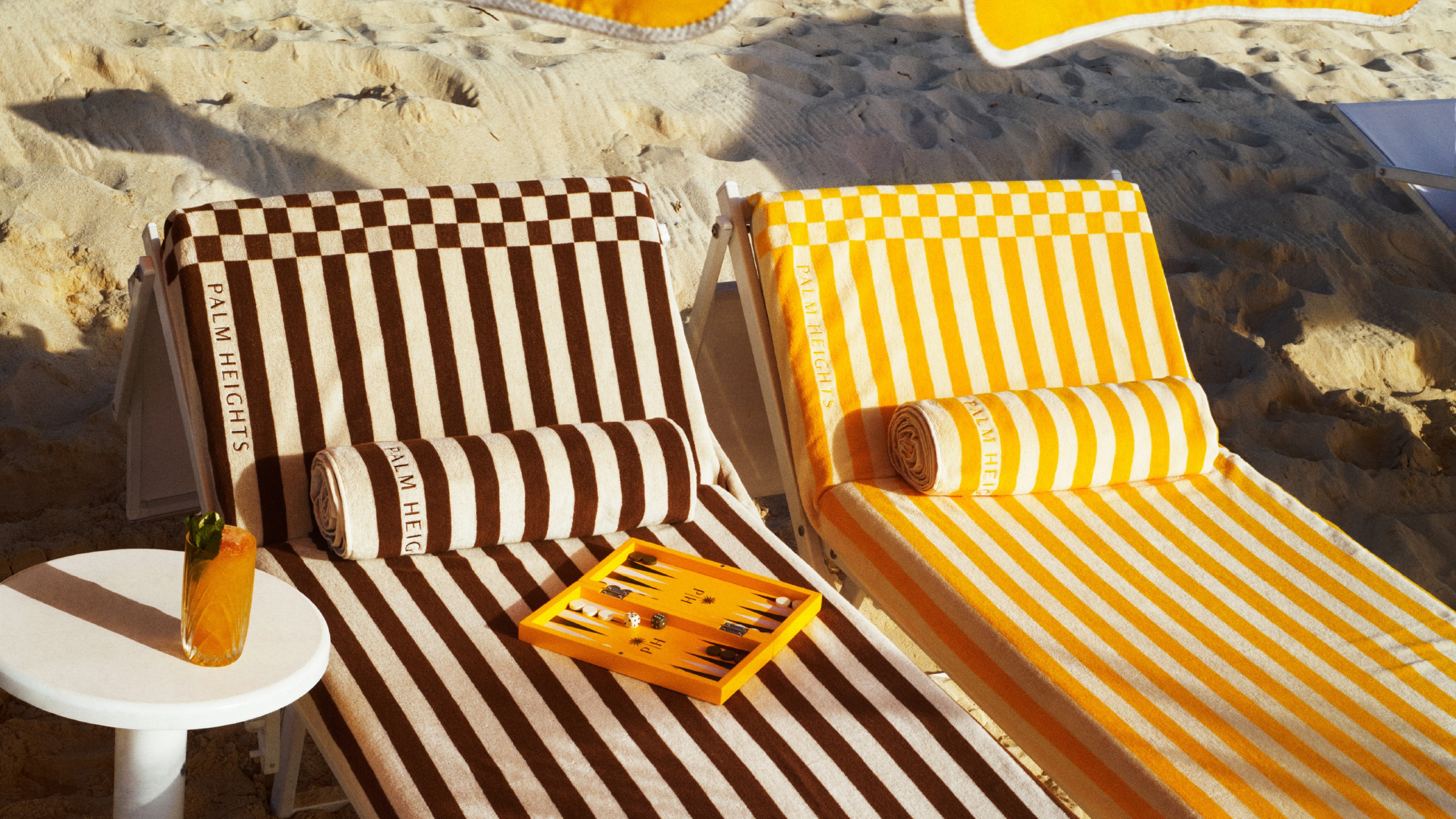 Two Palm Heights sun loungers covered in the striped towels from the H&M collection with the backgammon set on top