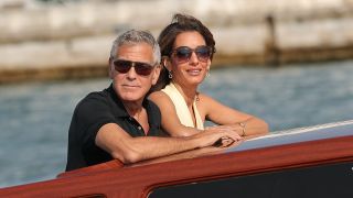 George and Amal Clooney relax on a boat with wind whipping through hair and sunglasses on at the Venice Film Festival 2025.