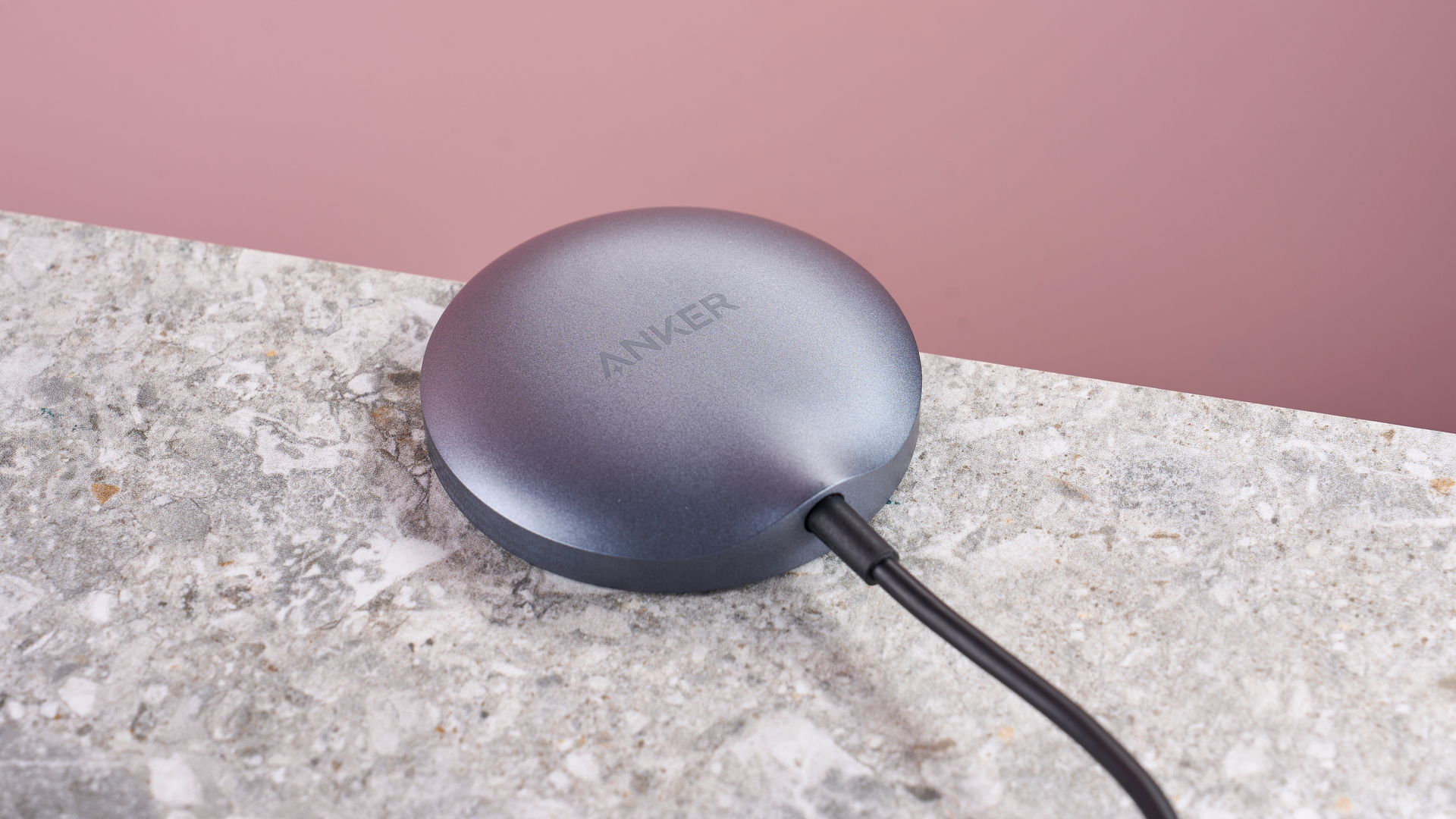 The back of the Anker Wireless Charging Pad. It is placed on a gray stone-like surface against a bright pink background.