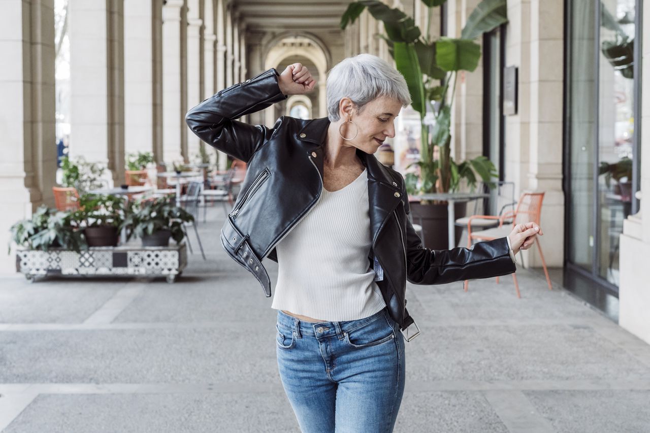 A mature woman struts down a street with a joyful air.