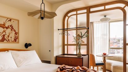 A modern rustic decorated hotel bedroom features rattan and warm textile finishes as well as a view over the city.