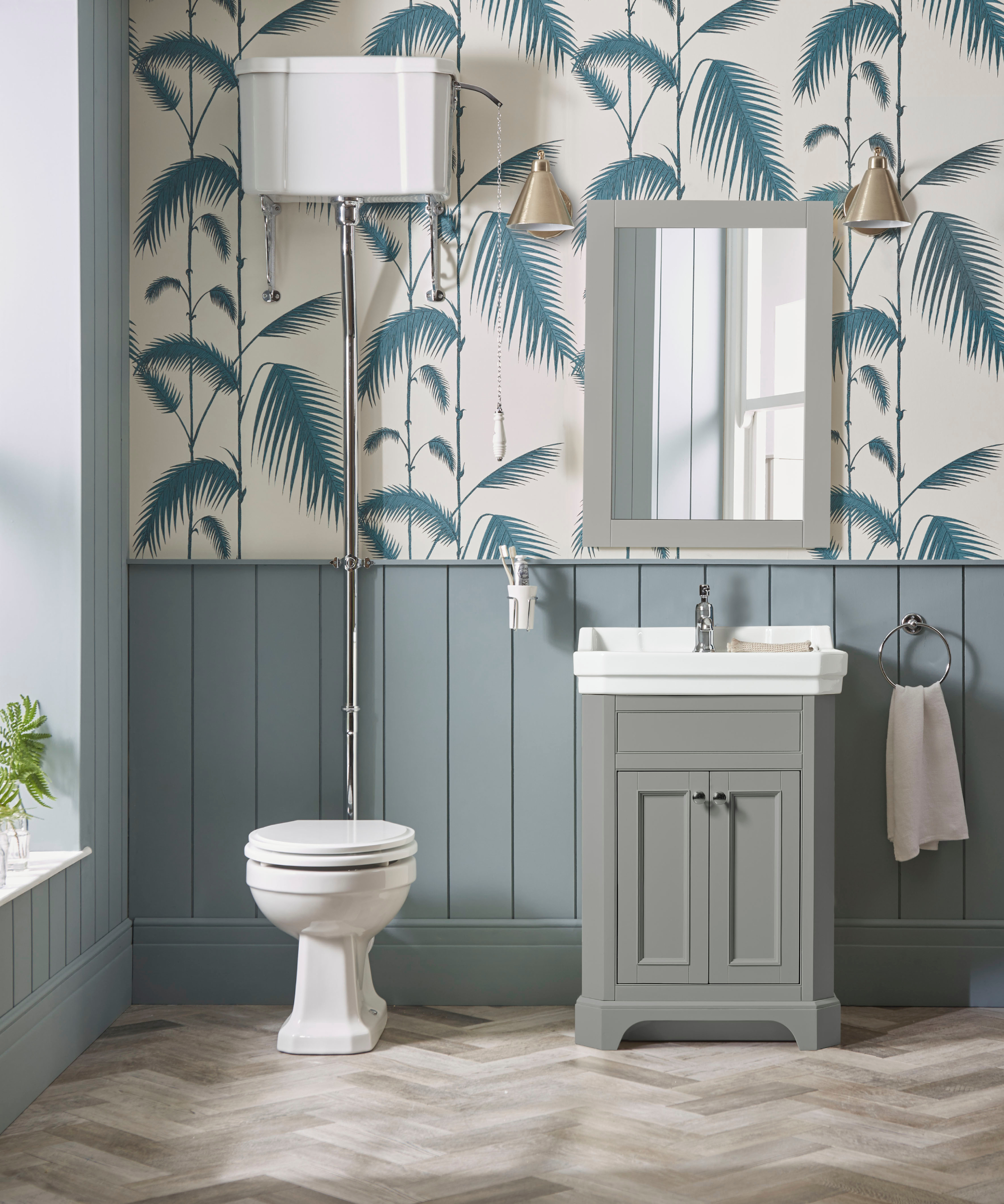 bathroom with grey wooden floor, painted blue wood panelling and leaf patterned blue and white paper above, grey vanity unit, mirror and white sanitaryware