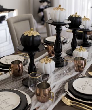 Halloween table decor with faux cobweb table runner and black and white pumpkins on cakestands