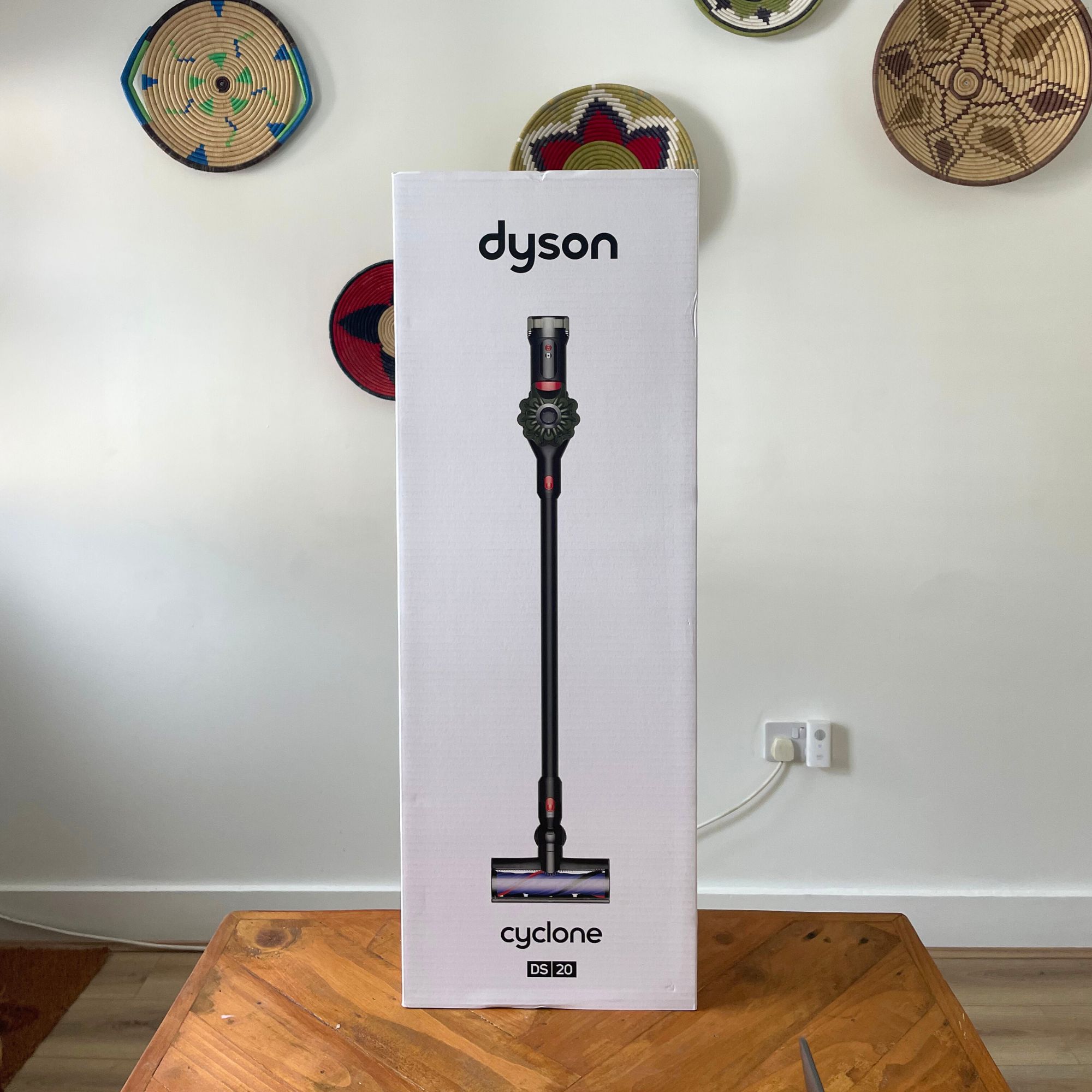 Dyson V8 Cyclone box sitting on a wooden table in front of a white wall with colourful baskets on it