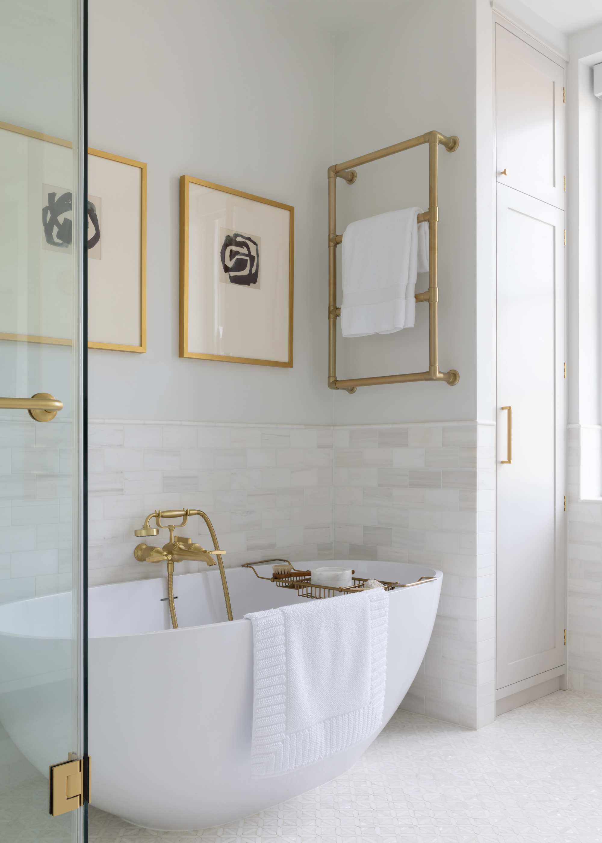 A modern traditional bathroom, with a contemporary bathtub, understated wall art above the tub and a towel rail in brushed brass to match the rest of the fixtures and fittings
