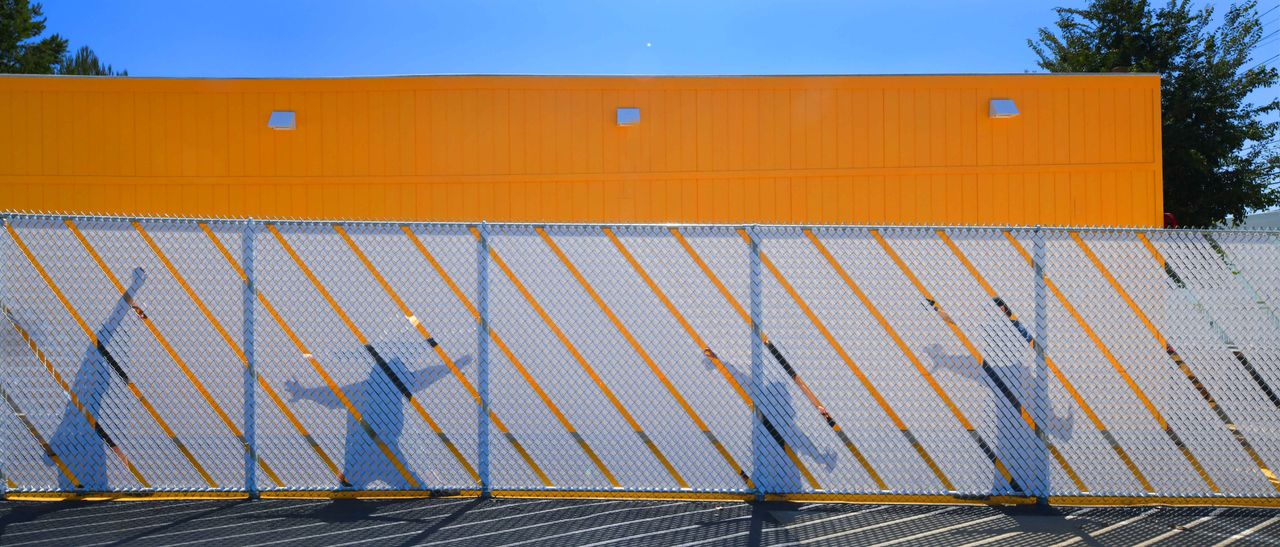 shadows of people on fence infront of an orange wall