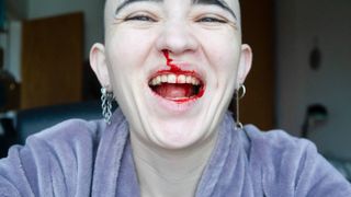 A close-up, joyful portrait of a person with a shaved head laughing broadly, with red liquid resembling blood smeared across their nose, lips, and teeth.