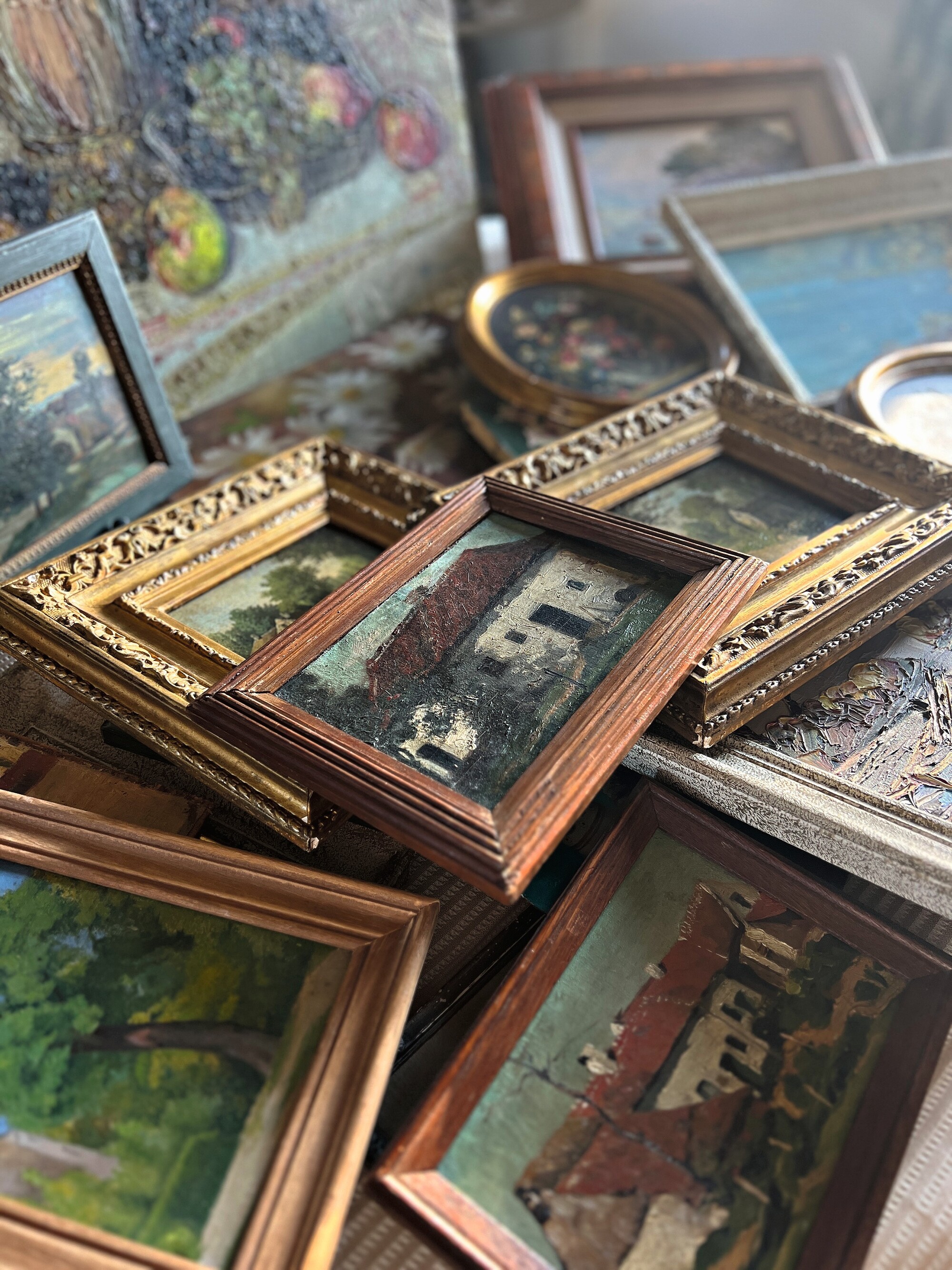 a selection on antique artworks in frames piled on a table