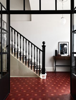 large black and white hallway with red floor tiles, with a black console table with art on top of it