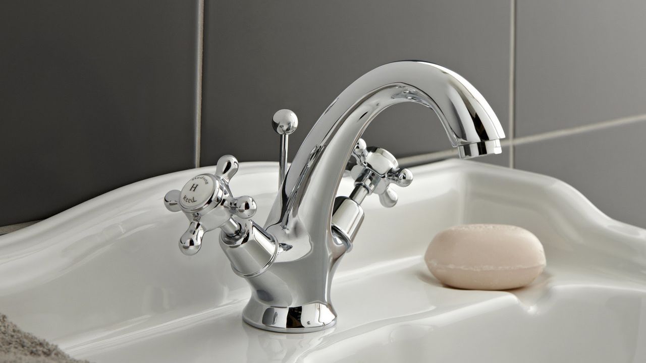 a silver tap, one of the best bathroom taps, on a white bathroom sink with a bar of soap next to it, against a grey tiled wall