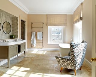 neutral bathroom with freestanding bath, tiled alcove and geometic print on wing chair in Georgian style Cotswolds newbuild country house